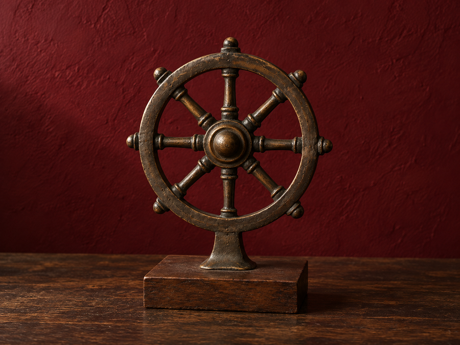 Eight-spoked bronze-coloured Dharma wheel on a wooden base against a dark red wall