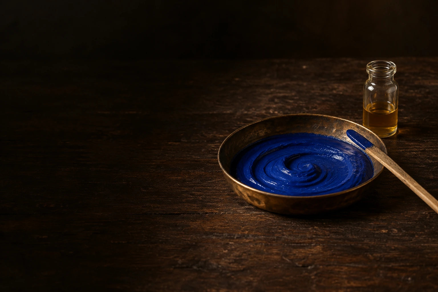 Lapis paint in a brass dish beside a vial of glue